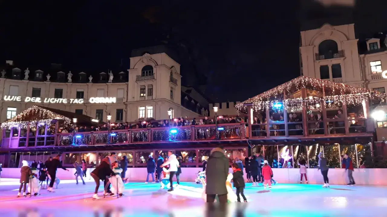 Eisbahn am Stachus Weihnachtsmarkt mit beleuchteten Buden und vielen Schlittschuhläufern.