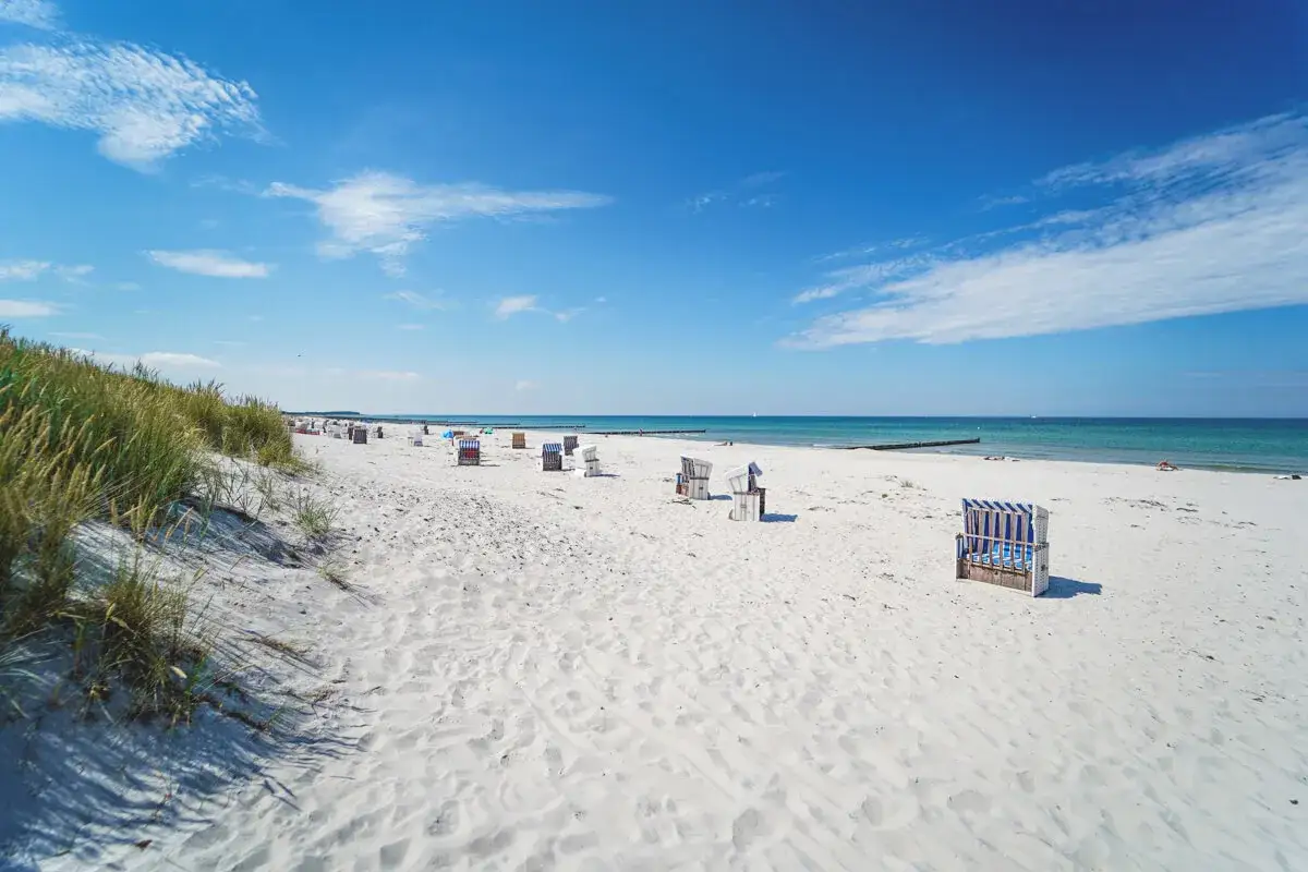 Hiddensee Strand mit Strandkörben und Dünen unter blauem Himmel.