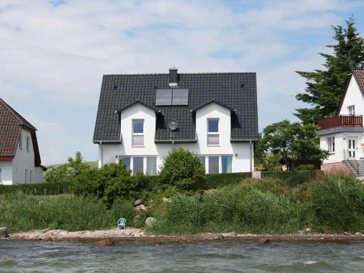 Moderne Häuser am Wasser in Neuendorf bei Putbus, umgeben von üppigem Grün.