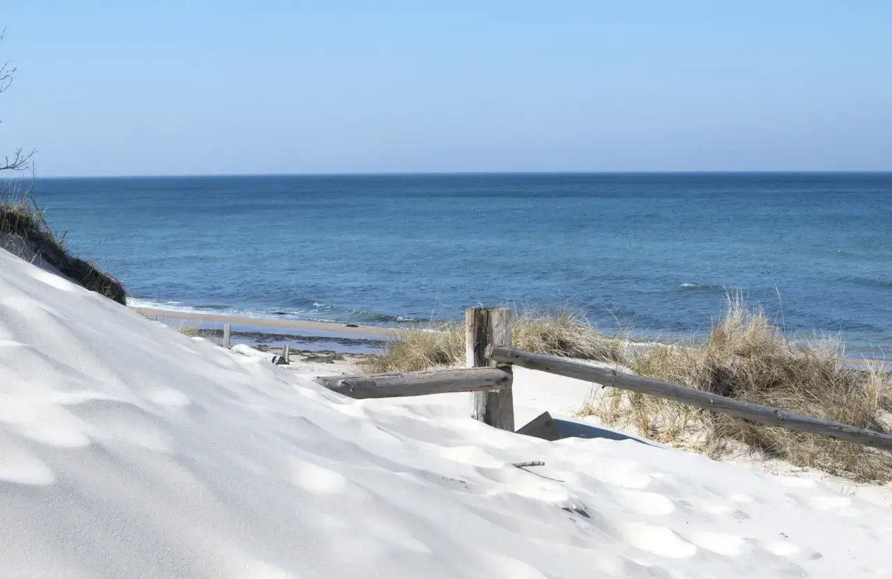 Weiße Sanddünen am Dranske Bakenberg, mit Blick auf das blaue Meer und den Himmel. Ein Holzzaun schützt die Vegetation.