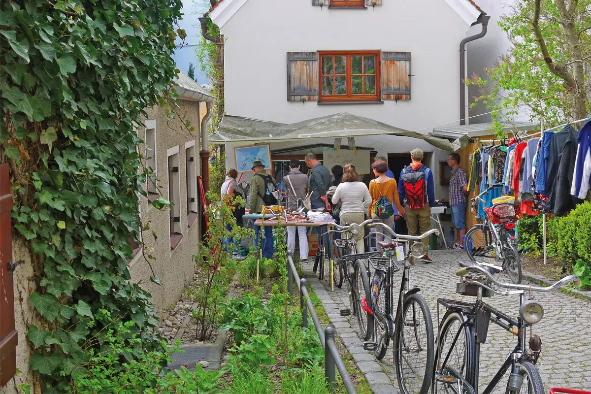Menschen stöbern auf einem Hofflohmarkt in Haidhausen zwischen Kleiderständern und Fahrrädern.