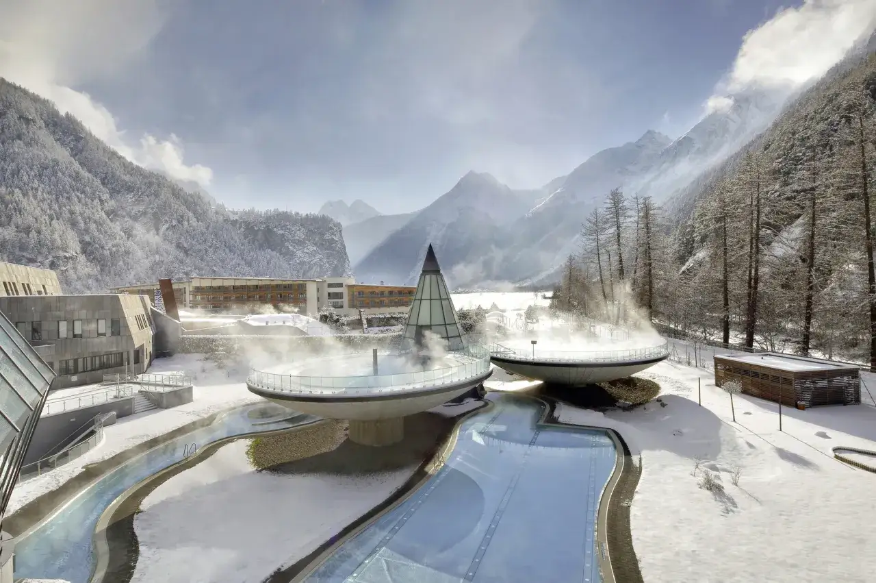 Traumhafte Winterurlaub Ideen: Ein modernes Spa mit beheizten Pools und Dampf vor schneebedeckten Bergen.