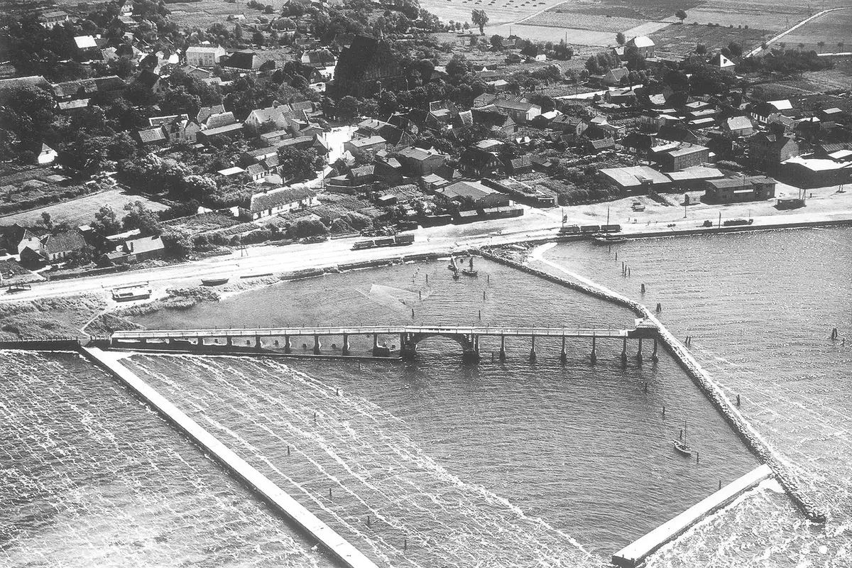 Luftaufnahme eines Dorfes an der Ostsee mit einer Brücke und einem Damm.