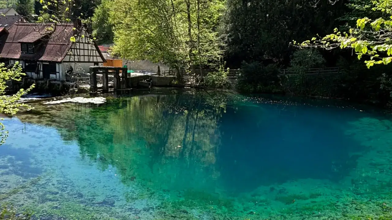 Der Blautopf in Blaubeuren, ein faszinierender Quelltopf mit tiefblauem Wasser, spiegelt die umliegende Natur und ein historisches Gebäude wider.
