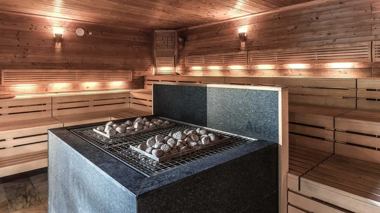 Gemütlicher Sauna bereich mit Holzbänken und einem Steinofen, bereit für entspannende Stunden.