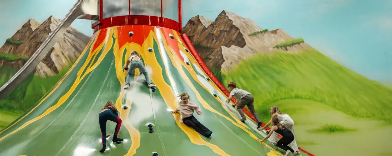 Kinder klettern an einer bunten Vulkanwand, eine tolle Idee für Unternehmungen bei Regen.