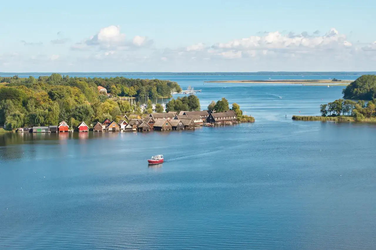Boote schaukeln im Wasser vor einer Reihe von Bootshäusern am Ufer der Mecklenburgischen Seenplatte.