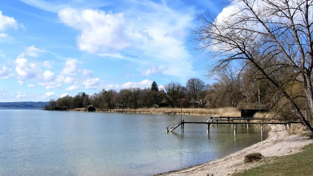 Am Ufer des Ammersees, mit Stegen und Bootshäusern, unter blauem Himmel mit Wolken.