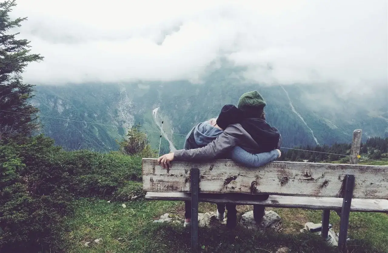 Zwei Personen kuscheln auf einer Bank und genießen die Aussicht auf die Berge. Eine schöne Idee, was man zu zweit unternehmen kann.