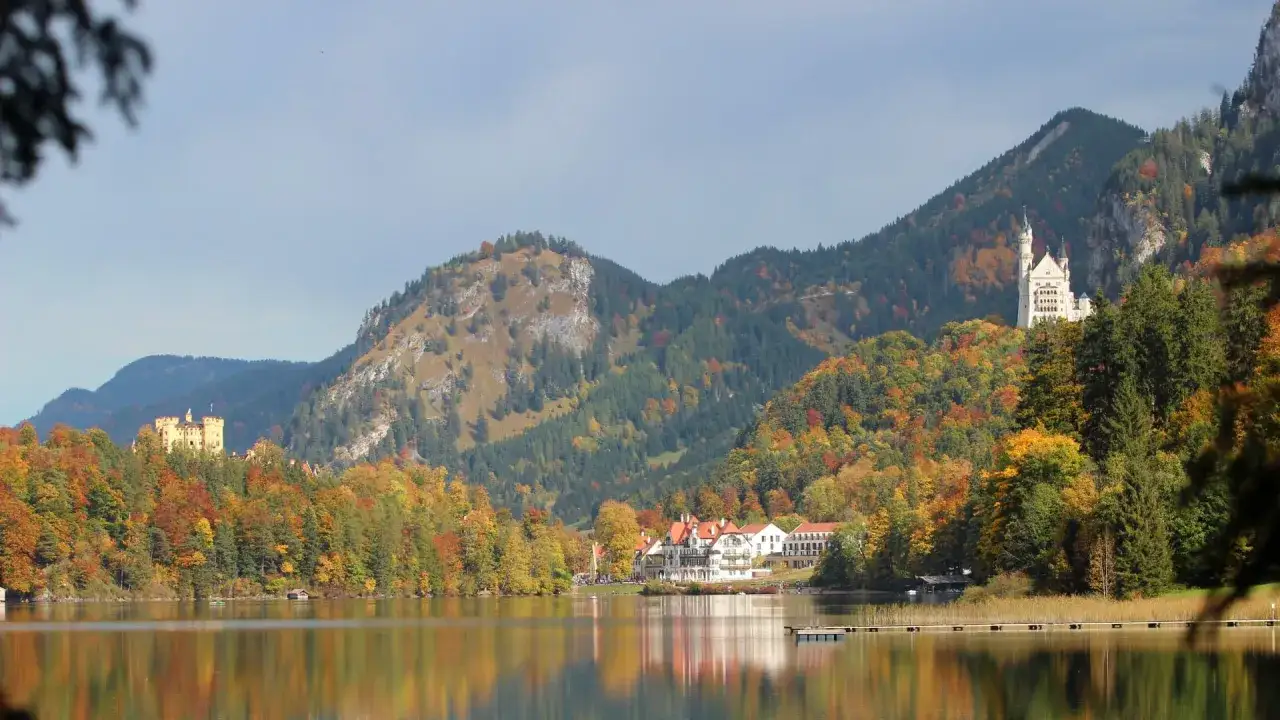 Herbstliche Unternehmungen in Bayern: Zwei Schlösser thronen auf bewaldeten Hügeln über einem spiegelglatten See.