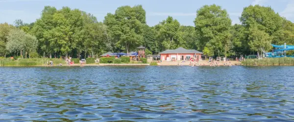 Sommerfreude an einem der **besten Badeseen Berlins**: Menschen planschen im Wasser, entspannen am Sandstrand und genießen die Sonne.
