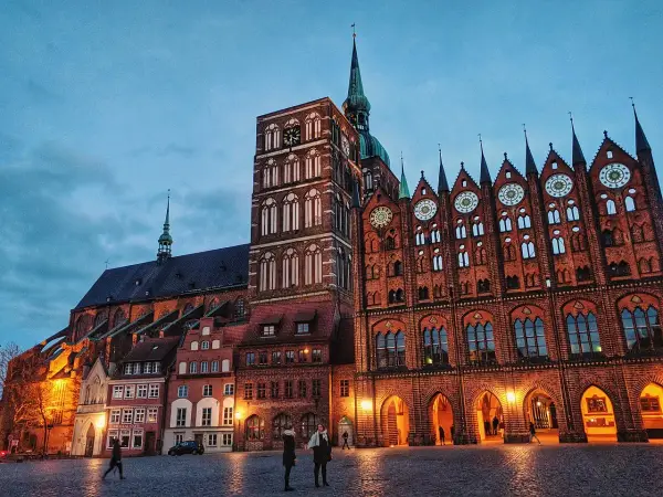 Abendstimmung im **Stralsund Zentrum**: imposante Backsteingotik mit Kirchturm und Rathaus, beleuchteter Marktplatz mit wenigen Passanten.