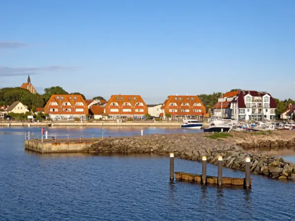 Hafen mit roten Ziegeldächern, Booten und einem Kirchturm im Hintergrund.