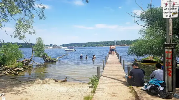 Sommer am ummanz strand: Menschen planschen im Wasser, andere sitzen am Steg. Ein sonniger Tag am See.
