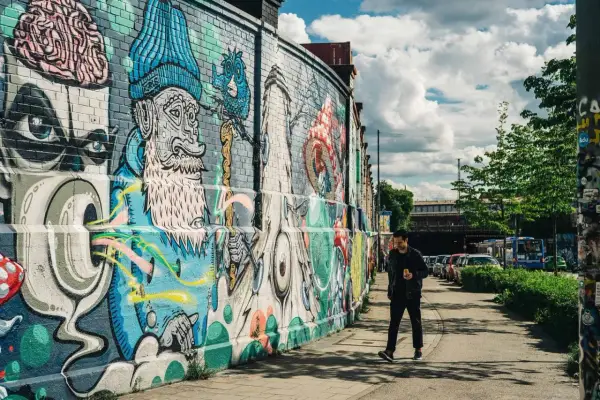 Mann geht an bunter Street Art in München vorbei. Die Wand ist mit fantasievollen Figuren und Mustern bemalt.