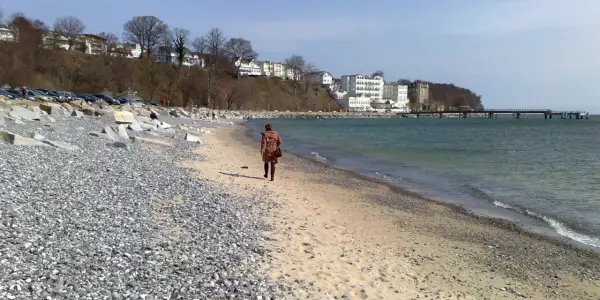 Eine Frau spaziert am Strand entlang, im Hintergrund die Bäderarchitektur von Sassnitz.